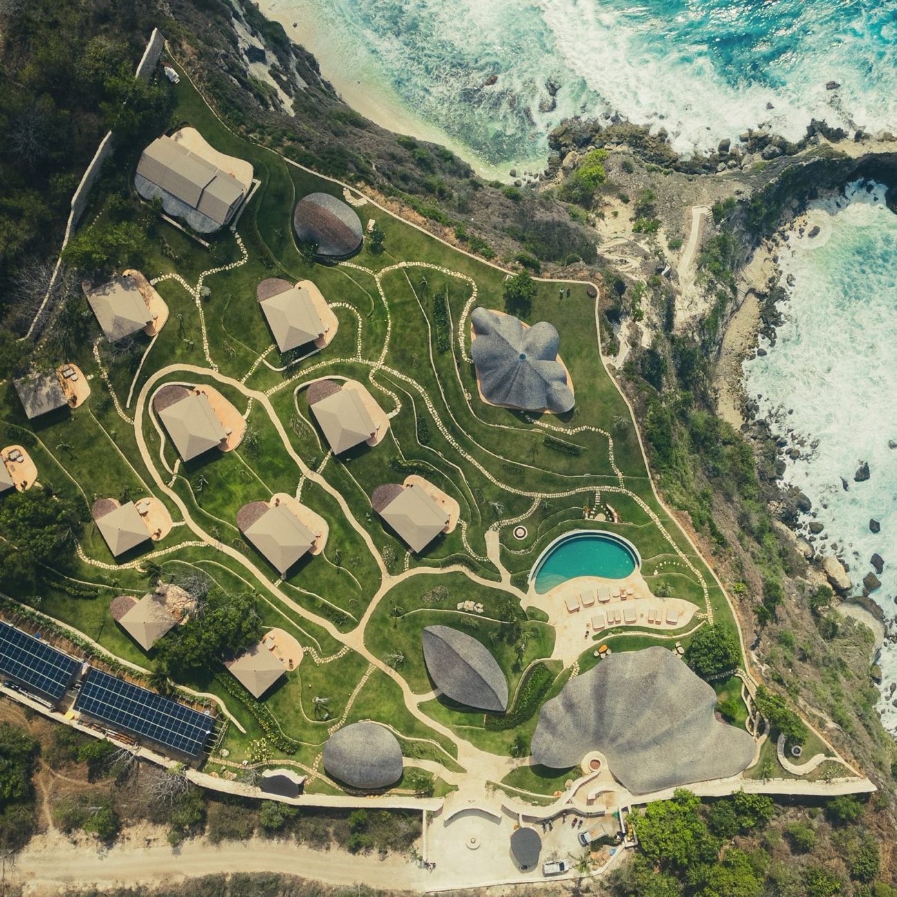 The retreat seen from above, shell roofed structures and tent suites set into the cliff above the ocean